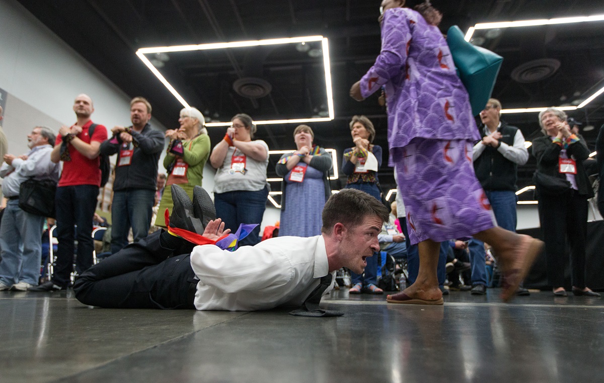 The Rev. Will Green lies on the floor of the 2016 United Methodist General Conference in Portland, Ore., with his hands and feet bound to protest the denomination's policies on human sexuality. Delegates returning from their lunch break passed by protestors on the floor and lining the entry to the meeting area. Photo by Mike DuBose, UMNS
