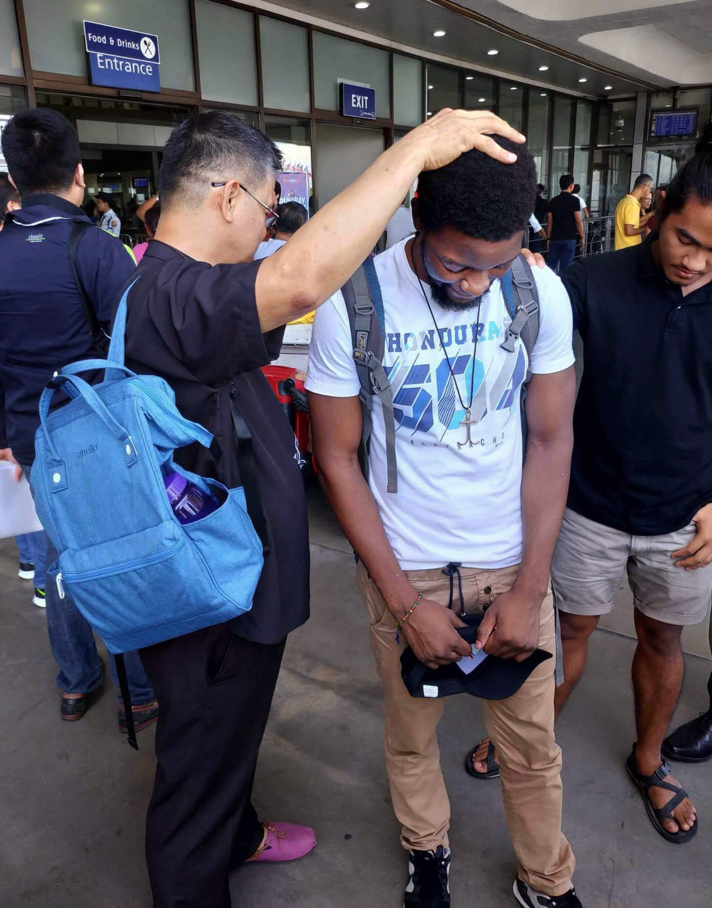 Bishop Ciriaco Q. Francisco (left) of the Manila Episcopal Area prays with Tawanda Chandiwana outside the Ninoy Aquino International Airport after the United Methodist missionary was released from a detention center and allowed to leave the Philippines. Photo by Mendoza Adrian.