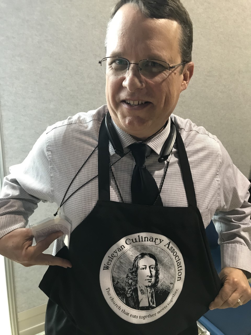 The Rev. John Feagins shows off a Wesleyan Culinary Association apron on Feb. 23. He’s among many observers at the 2019 General Conference in St. Louis, and he’s been in the corridors of America’s Center, talking to delegates and others about how food can be a bridge for people with different theological views. The Wesleyan Culinary Association is a Facebook group which shares potluck and communion bread recipes. Photo by Sam Hodges, UMNS.