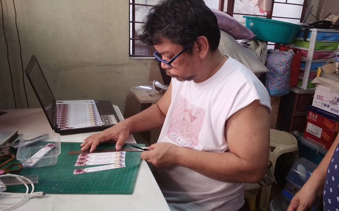 Melvin Nor S. Ramos, un laïc de l'église Méthodiste Unie de Kawan ni Kristo, dans le district de Bulacan Sud aux Philippines, travaille sur des étiquettes pour ses masques. Avec sa famille et d'autres membres de l'église, il a mobilisé des ressources pour créer la protection nécessaire pour les hôpitaux et les centres de santé locaux dans la lutte contre le coronavirus. Photo avec l'aimable autorisation de Melvin Nor S. Ramos.