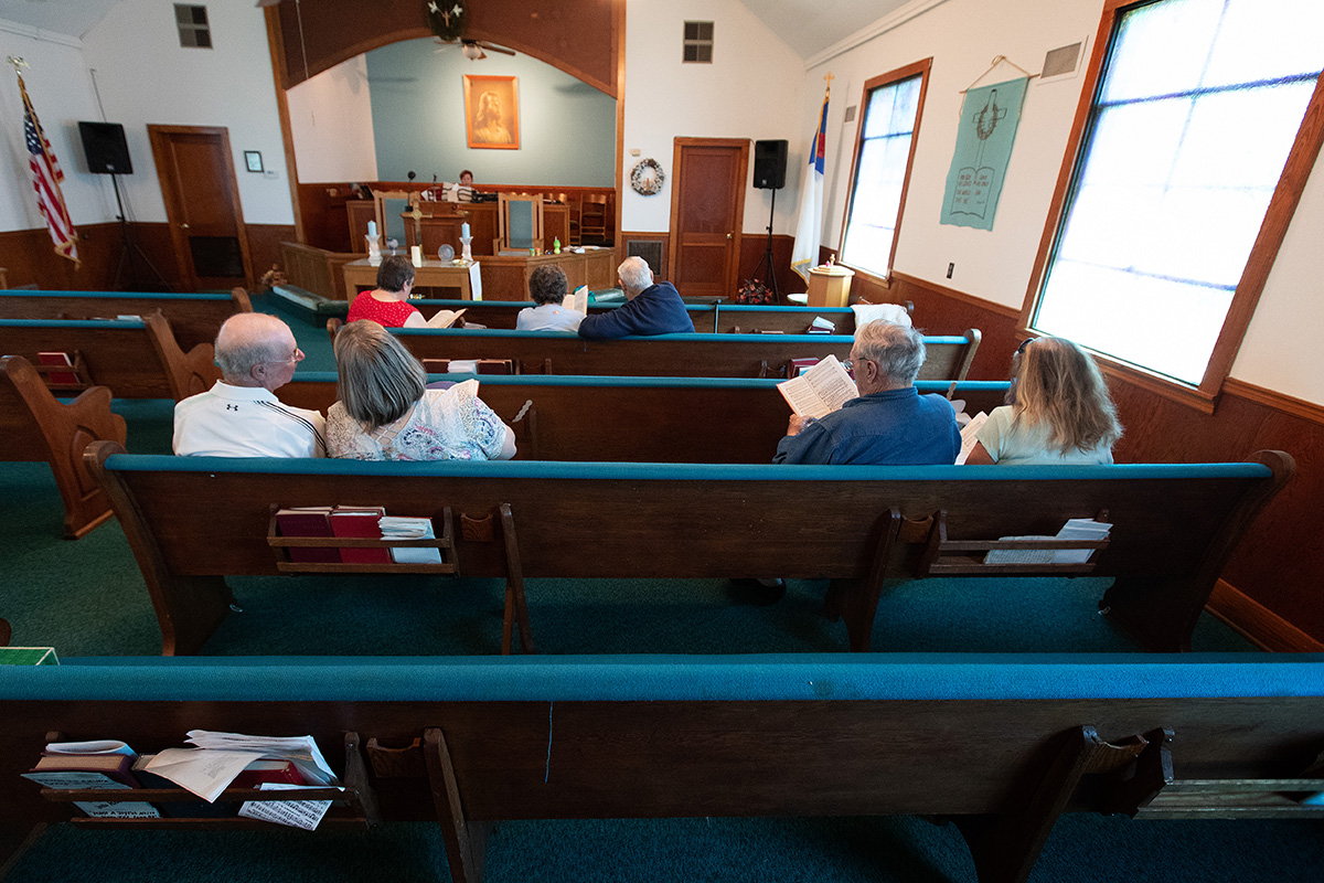 Uma congregação de sete pessoas canta durante o culto na Igreja Metodista Unida Oakton fora de Clinton, Ky. A Pastora Laura Vincent toca piano atrás do altar. As pequenas igrejas rurais lutaram contra a pandemia do coronavírus, mas muitas delas agora estão aproveitando o retorno aos cultos pessoais e olhando para o futuro. Foto Mike Dubose, Notícias MU.