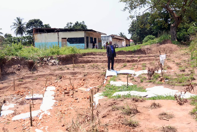 Le Révérend Kelly Yimbi Mbo dans une géante érosion remplie après les travaux effectués les Méthodistes Unis dans le District de Kananga. Les travaux effectués par les Méthodistes Unis ont permis de sauver des églises, établissements scolaires et autres bâtiments appartenant à l’église qui étaient menacés de destruction par les géantes érosions sur ce lieu. Photo par Serge Mukendi, UM News.