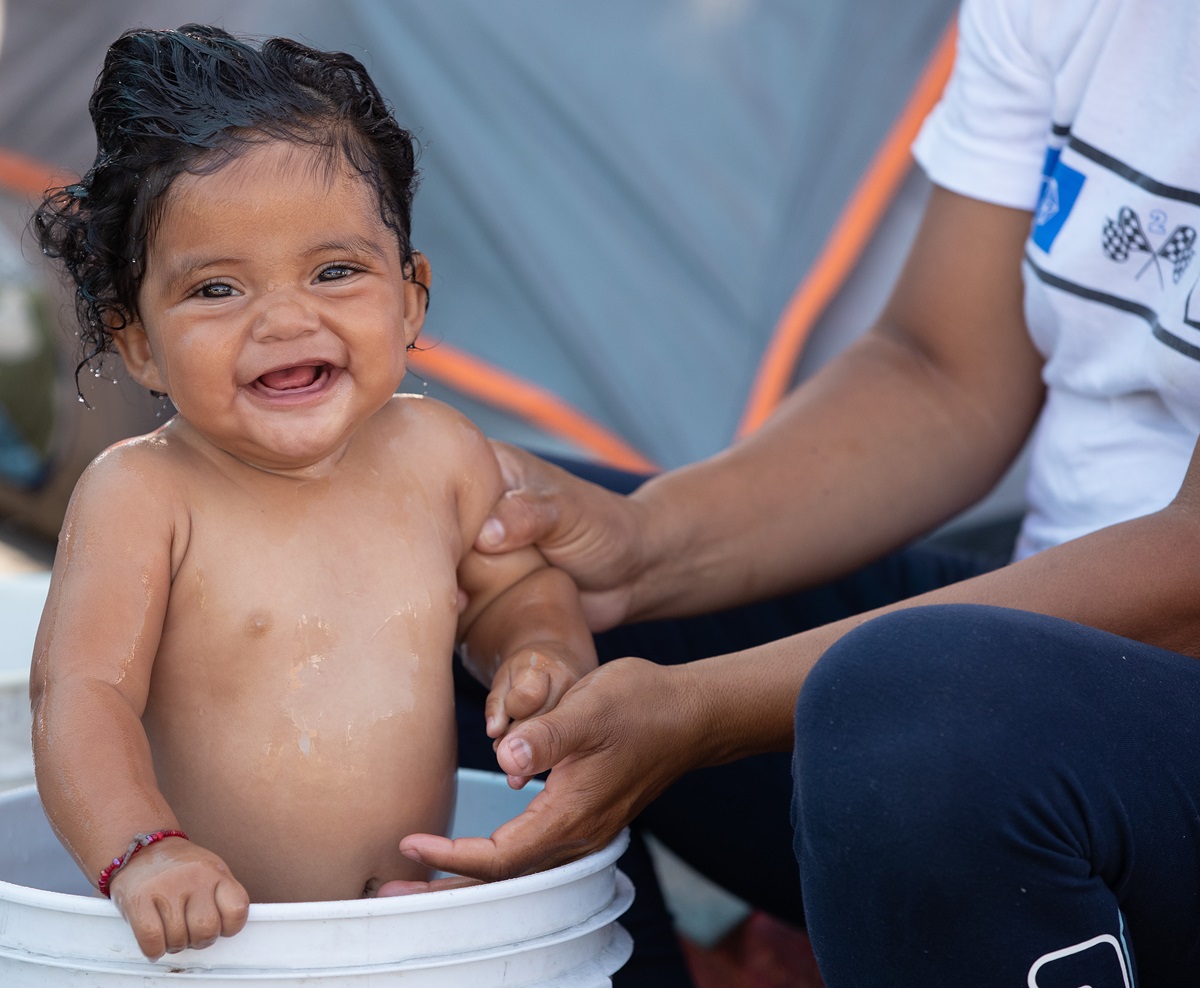 Kelani, de 8 meses, cuya madre huyó de la violencia de las pandillas en Honduras, se baña en un balde de plástico en un campamento improvisado para migrantes en el cruce fronterizo El Chaparral en Tijuana, México. Miles de niños y niñas nacen en la peregrinación que los migrantes siguen hacia las fronteras en búsqueda de esperanza y futuro. Foto de Mike DuBose, UM News. Kelani, de 8 meses, cuya madre huyó de la violencia de las pandillas en Honduras, se baña en un balde de plástico en un campamento improvisado para migrantes en el cruce fronterizo El Chaparral en Tijuana, México. Miles de niños y niñas nacen en la peregrinación que los migrantes siguen hacia las fronteras en búsqueda de esperanza y futuro. Foto de Mike DuBose, UM News.