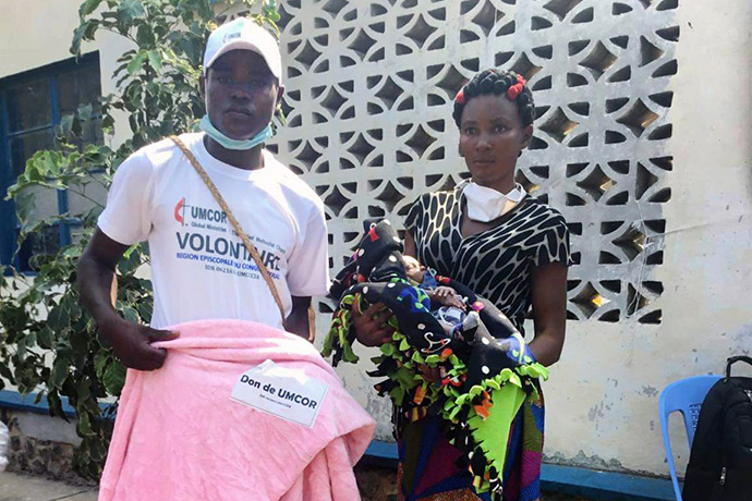 Madame Ortance Tshikonga 38 ans et l'un des volontaires qui l’a aidé à transporter ses vivres et non vivres après la réception. Tshikonga  est veuve et Mère de quatre enfants. Plus de 415 familles constituées de plus de 2 490 personnes expulsées de l’Angola, ont bénéficié de la nourriture et vêtements, une assistance de l’Eglise Méthodiste Unie. Photo du Pasteur Serge Mukendi, UM News.