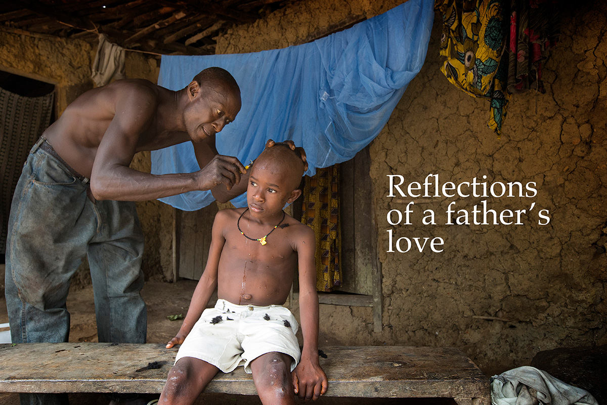 Peter Braima gives his son, Moses, a haircut with a safety razor at their home in Manjama village, near Bo, Sierra Leone, in 2014, while their new, insecticide-treated mosquito net airs out behind them. The nets were provided by The United Methodist Church's Imagine No Malaria campaign. Photo by Mike DuBose, UM News.