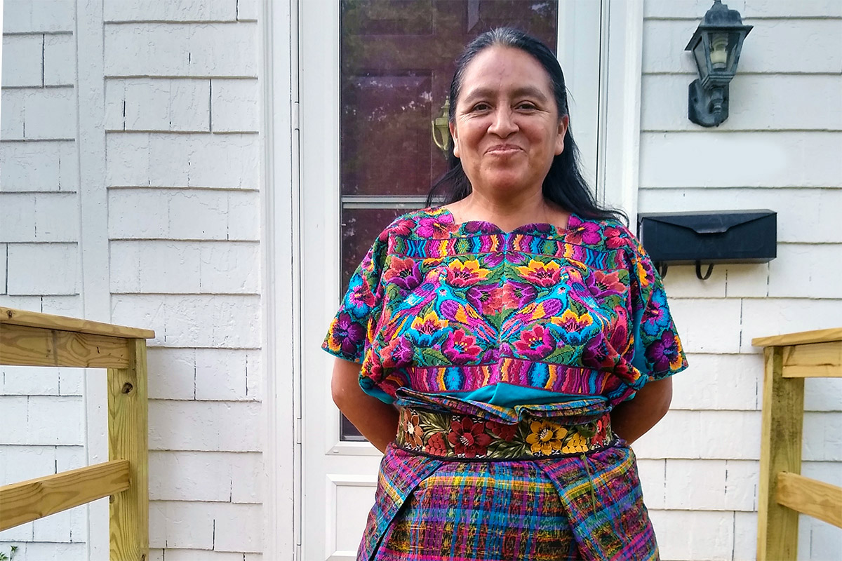 Maria Chavalan Sut frente a la casa de tres habitaciones que alquila con sus cuatro hijos en Charlottesville, Virginia. Chavalan Sut huyó de su Guatemala natal en 2015 y pasó tres años en el santuario de la Iglesia Metodista Unida Memorial Wesley antes de recibir una suspensión de su proceso de deportación en 2021. Foto cortesía de Richard Lord.