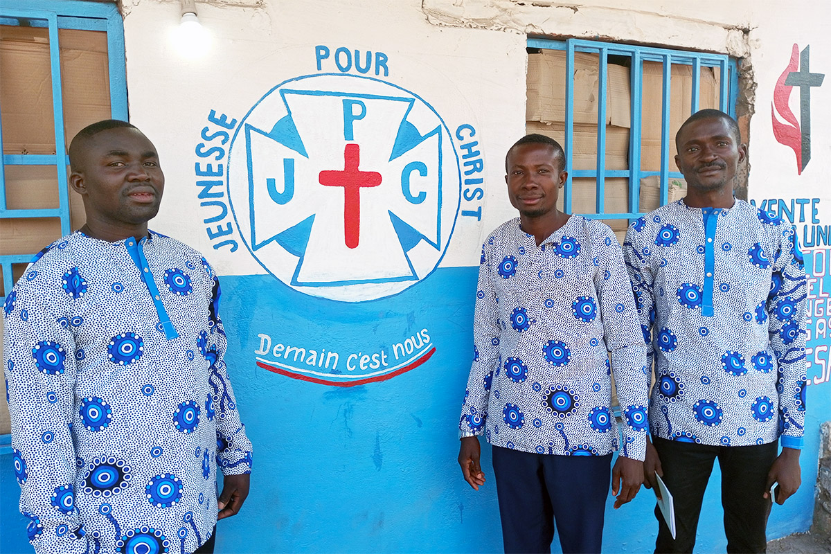 Des responsables actuels et anciens du comité des jeunes de la Kabondo Center United Methodist Church se tiennent devant la boutique de l'église qu'ils gèrent pour générer des revenus pour les jeunes de Kabondo, au Congo. William Ilunga Mushimukata, Ngulu Mingi et Hugo Banza Kyakulomba (de gauche à droite). Photo par la Révérende Betty Kazadi Musau, UM News.