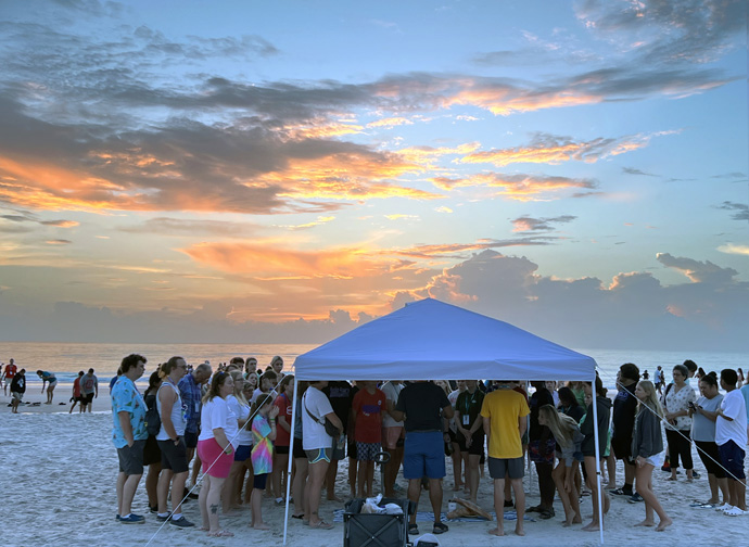 Dezenas se reúnem sob uma tenda para a comunhão ao nascer do sol durante o Youth 2023, realizado em Daytona Beach, Flórida, de 25 a 28 de julho. Representantes de 12 das 13 agências da Igreja Metodista Unida participaram como oradores, líderes de workshops e expositores. Foto de Crystal Caviness, Comunicações Metodista Unida. 