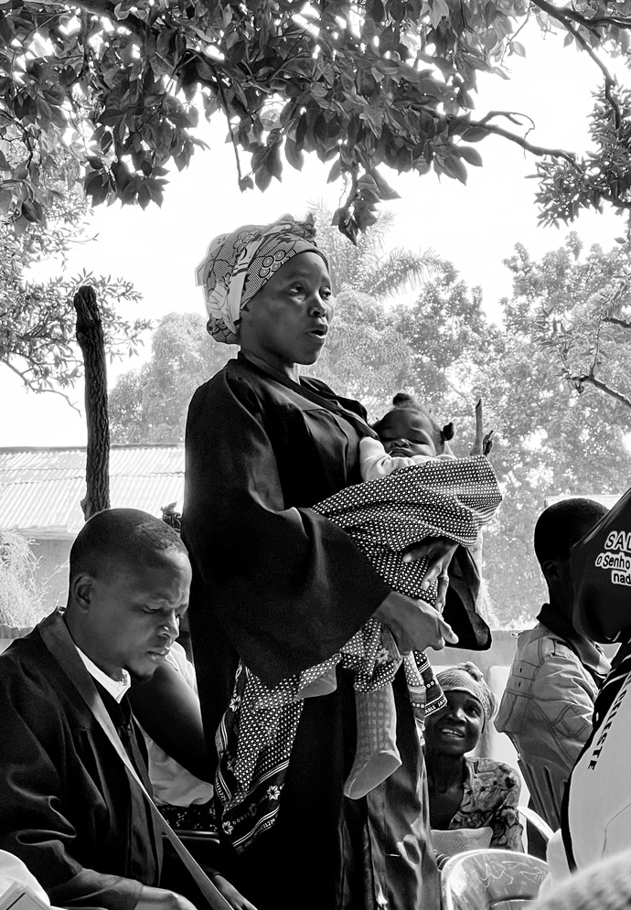 Um membro clerical segura o seu filho pequeno quando ela se apresenta na reunião do Distrito de Quela no Leste de Angola. Em Julho, uma equipe de missão da Conferencia de Mountain Sky reuniu-se com pastores Metodistas Unidos nas aldeias da Conferência do Leste de Angola para saber de que maneira eles poderiam fornecer apoio. Foto cedida pelo Rev. Jared Stine.