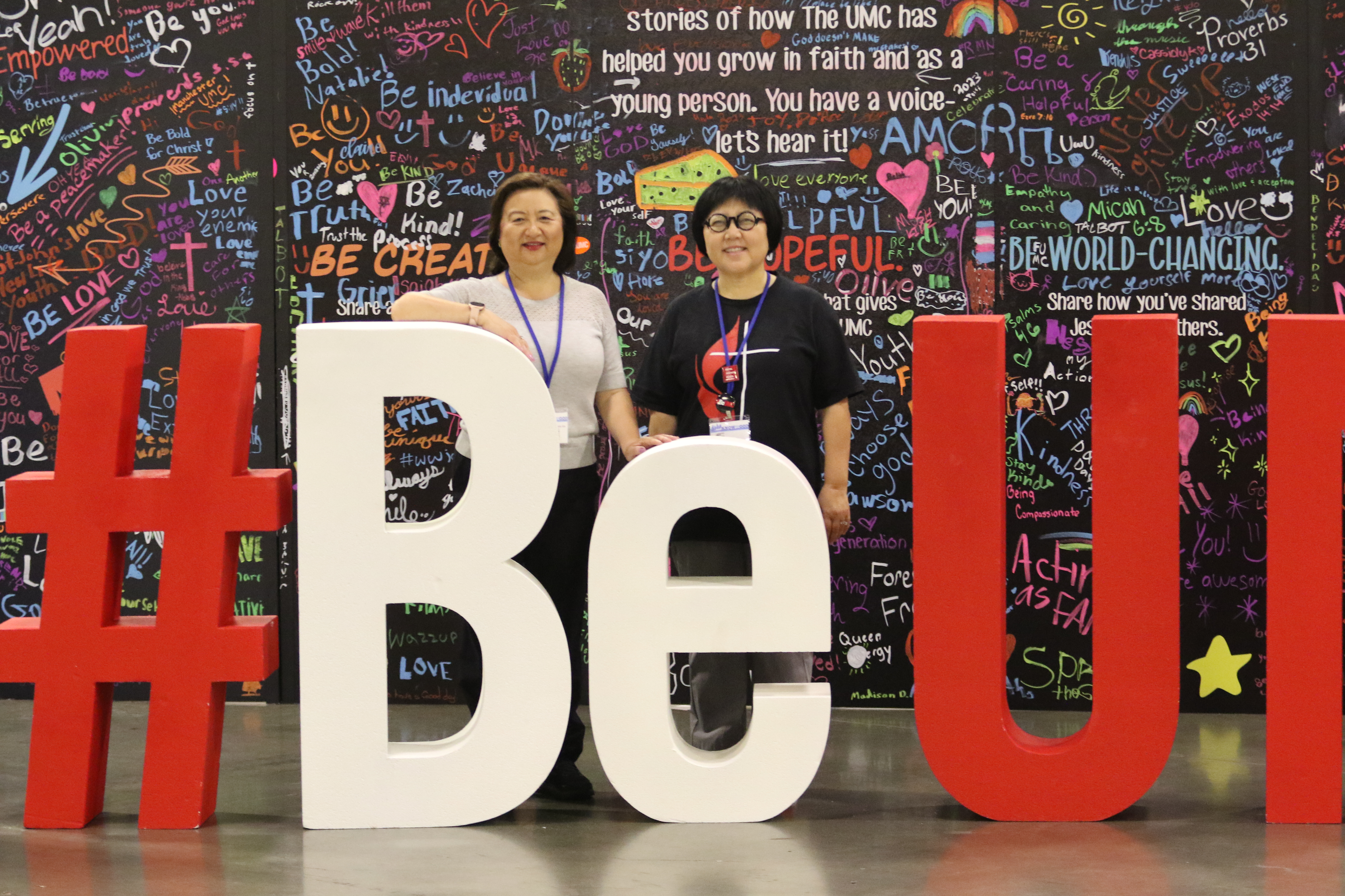 산드라 보넷-김 목사와 서니 안 목사가 총회 #BE UMC 사인 뒤에 서 있다. 사진, 김응선 목사, 연합감리교뉴스.