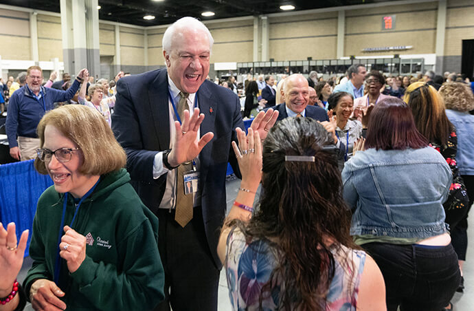 Bishop Thomas J. Bickerton high-fives delegates, visitors and staff of the United Methodist General Conference in Charlotte, N.C., who are dancing in the aisles following morning worship on the final day of the conference. Behind him is Bishop John Schol. Photo by Mike DuBose, UM News.