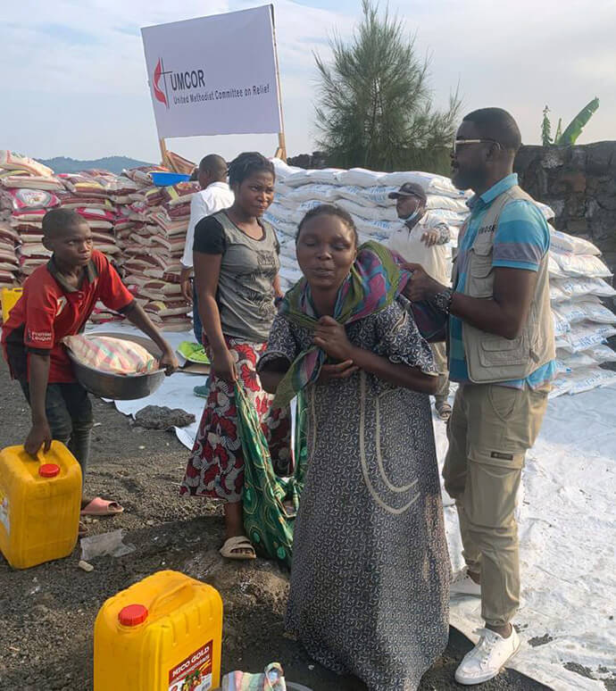 John Lusulu, financial assistant with the United Methodist Committee on Relief’s disaster management office in eastern Congo, helps a young woman carry food during a distribution operation for people displaced by war in Goma, Congo. Each household received one month’s food aid and essential non-food items. Photo by Chadrack Tambwe Londe, UM News.