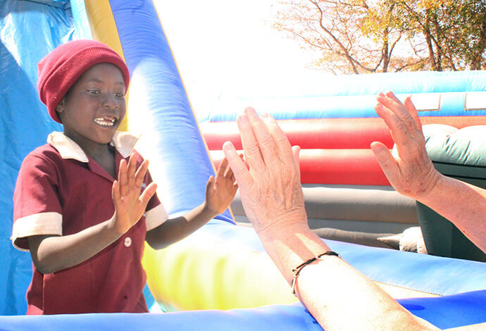 Mavis Turuside, élève de première année, tape dans la main de Barbara Julian, bénévole, au bas d'un toboggan. Photo par Kudzai Chingwe, UM News.