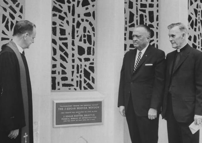  J. Edgar Hoover (centro), diretor do FBI, fica ao lado de uma placa dedicando um grande vitral a ele na Igreja Metodista Capitol Hill, hoje chamada Igreja Metodita Unida Capitol Hill, em 26 de junho de 1966. Também na foto estão o Rev. Edward B. Lewis (esquerda), pastor da igreja, e o Rev. Frederick Brown Harris (direita), capelão do Senado. A janela está programada para ser rededicada em 29 de setembro para diminuir a conexão com Hoover, cuja casa de longa data ficava no que hoje é o estacionamento da igreja. Foto cortesia da IMU Capitol Hill. 
