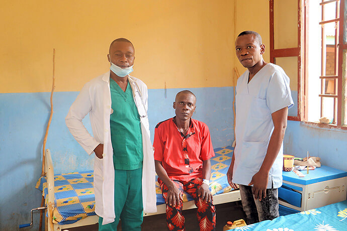 Mukindji Mpoyo (en chemise rouge) pose avec le Dr Pierre Omesombo (à gauche), médecin traitant, et une infirmière de l'Hôpital Général de Tunda à Tunda, au Congo. Mpoyo a parcouru 200 kilomètres pour être soigné dans l'établissement méthodiste uni. Photo par Chadrack Tambwe Londe, UM News.
