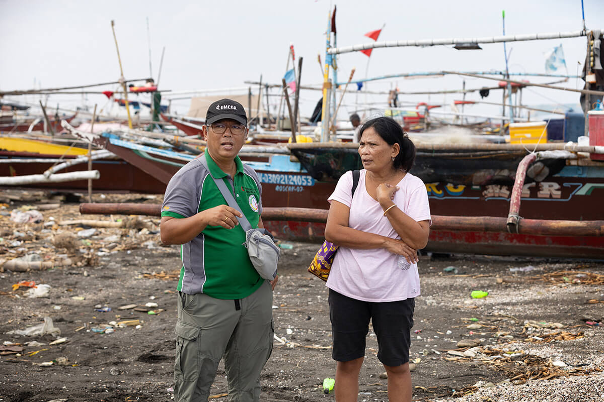 Emma Asores (right) and Romuel “Dojoe” Flores walk among idled fishing boats in the Mozon II neighborhood in Rosario, Philippines. Typhoon Carina caused three oil tankers to sink in July, prompting the government to ban fishing in villages around Manila Bay. The United Methodist Church distributed rice to affected families in Tanza and Rosario in Cavite Province. Asores heads the women’s organization in Mozon II and Flores is a consultant with the United Methodist Committee on Relief’s International Disaster Response unit. Photo by Mike DuBose, UM News.
