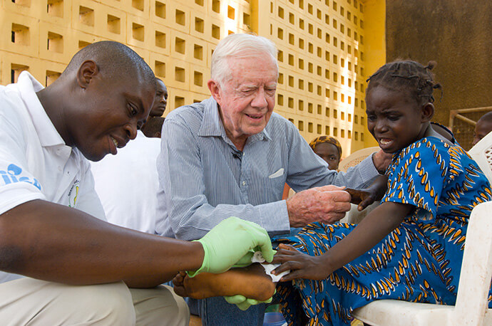 Jimmy Carter réconforte une jeune patiente à qui l'on a retiré un ver du corps à Savelugu, au Ghana, en février 2007. Le Centre Carter mène la campagne internationale d'éradication de la dracunculose. Photo avec l'aimable autorisation du Centre Carter.