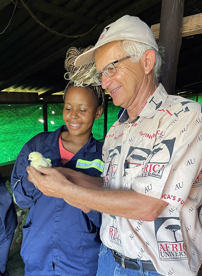 O missionário Larry Kies e Audrey, uma estudante da África University, admiram um pintainho de um dia na Machamba dos Sonhos da escola, onde Kies serviu como professor e consultor técnico. Foto cedida por Larry Kies.