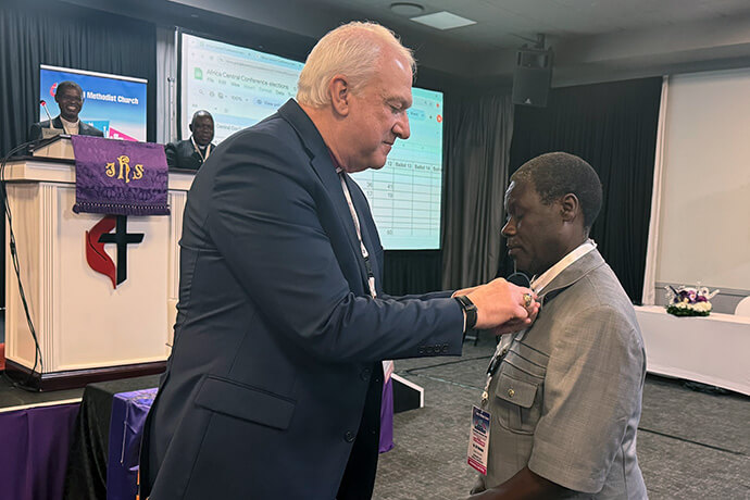 L'évêque Thomas Bickerton épingle l'insigne épiscopal méthodiste uni sur le col du révérend Gift Machinga. La Conférence Générale de l'année dernière a élu le révérend Machinga membre du Comité Permanent pour les Questions Relatives à la Conférence Centrale. Photo par Priscilla Muzerengwa, United Methodist Communications.