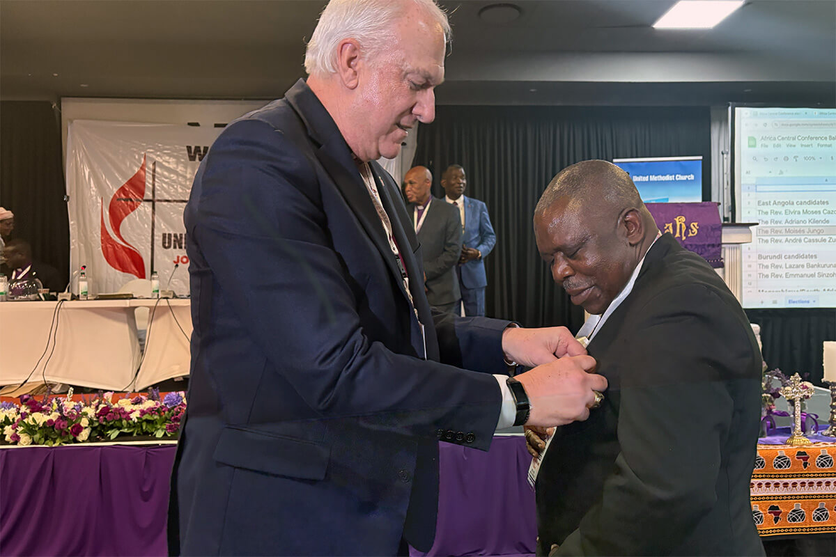 O Rev. Moisés Bernardo Jungo (à direita) recebe o broche episcopal do Bispo Thomas Bickerton após ser eleito bispo Metodista Unido em 15 de março na Conferência Central da África em Joanesburgo. O pastor de Angola foi o segundo bispo eleito na Conferência. Foto de Eveline Chikwanah, Notícias MU.