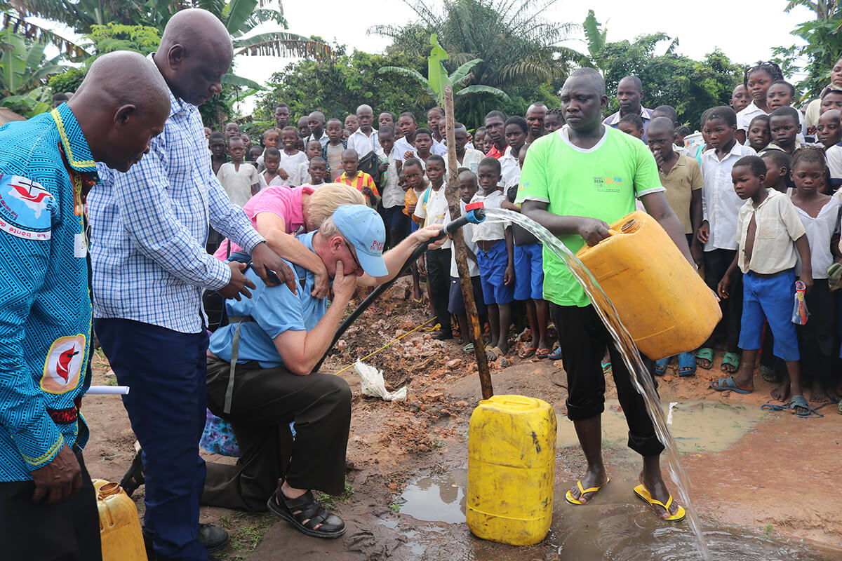 The Rev. Jonathan Baker and Donna Baker are overwhelmed as water gushes forth from a well in Wembo Nyama, Democratic Republic of Congo, in 2016. The local people had been praying for water for decades. New Covenant United Methodist Church in The Villages, Fla., and its Lake Deaton United Methodist Church campus in Wildwood, Fla., raised the money for this first well in the Sankuru Province of Central Congo. Photo by the Rev. Jim Divine.