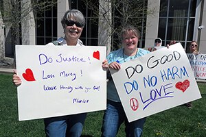 Cheryl Lowe and Andrea Gauldin-Rubio, both United Methodists, hold their signs based on Scripture and the teachings of John Wesley at the Hands Off! rally on April 5 outside the courthouse in Waynesville, North Carolina. They were among many United Methodists who used their lunchtime during the nearby Peace Conference to attend the nonviolent rally decrying government overreach. Lowe is a member of Mt. Pleasant United Methodist in McLeansville, N.C., and Gauldin-Rubio is the director of Christian education at Bunker Hill United Methodist Church in Kernersville, N.C. Photo by Heather Hahn, UM News.