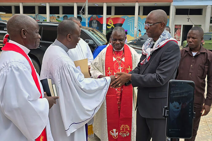 O vice-governador Franco Mufinda (usando terno preto), Saúde oficiais da Conferência à sua Chegada, da direita para esquerda Bispo Moisés Bernardo Jungo com a Stola episcopal, a esquerda saudando Mufinda, Rwv. Rogerio Bartolomeu, Assistente do Bispo, e de seguibda Rev. Pedro Gouveia, Superitendente do Distrito de Malange. Foto de Orlando da Cruz, Notícias da MU. 