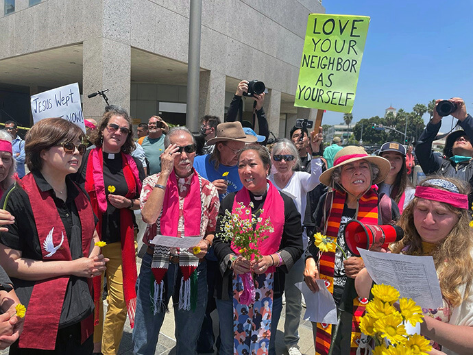 Pastors, rabbis and lay people join in a June 10 prayer vigil organized by Clergy and Laity United for Economic Justice outside a federal building, where ICE has its offices in Los Angeles. At center holding flowers is the Rev. Allison Mark, president of the United Methodist Board of Church and Society and senior pastor of Faith United Methodist Church in Torrance, Calif. Photo courtesy of Clergy and Laity United for Economic Justice. 