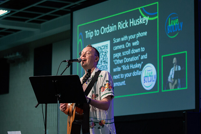 Brian Schroeder leads a song with a theme of pride and acceptance at the 2025 Minnesota Annual Conference at the River’s Edge Conference Center in St. Cloud, Minn., on June 13 as an offering was collected to support travel expenses for Bishop Lanette Plambeck to visit and ordain Dr. Richard Huskey. Photo courtesy of the Minnesota Conference.