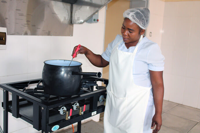 Winnet Nyamuda, cuisinière à l'hôpital Nyadire Mission Hospital au Zimbabwe, s'occupe d'une casserole sur la cuisinière alors qu'elle prépare un repas pour les patients. Nyamuda a exprimé sa gratitude pour la rénovation de la cuisine rendue possible par le Conseil Méthodiste Uni des Ministères Mondiaux. Photo de Kudzai Chingwe, UM News.