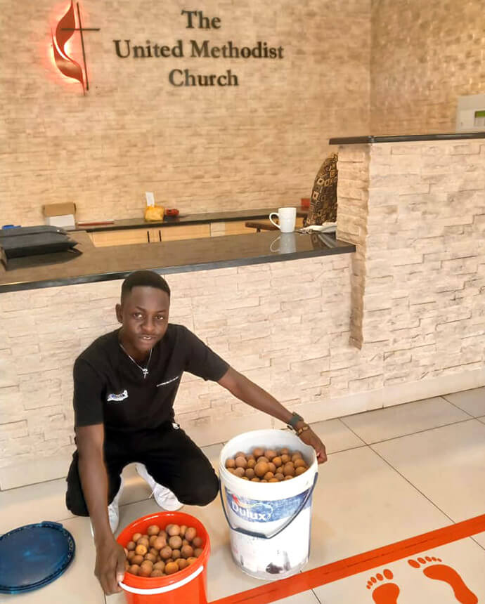 Panashe Banda, diplômé de Africa University, montre des seaux de mazhanje, un fruit sauvage africain, qu'il a apporté comme cadeau au personnel du siège de la Conférence de l'Ouest du Zimbabwe. Banda partage chaque année la récolte de sa famille avec le personnel en guise de remerciement pour la bourse d'études qu'il a reçue de l'Eglise pour étudier à l'université méthodiste unie de Mutare, au Zimbabwe. Photo par Chenayi Kumuterera, UM News.