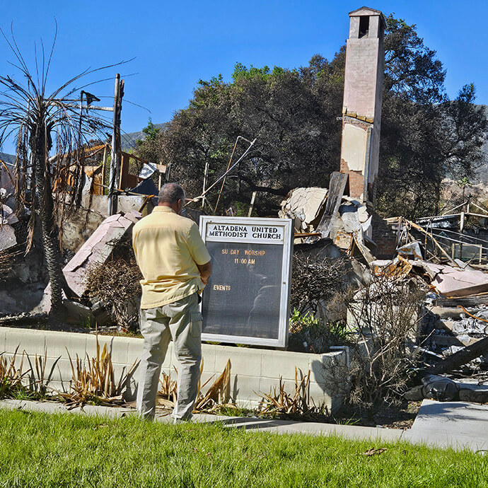 A visitor reads Altadena United Methodist Church’s sign in front of the church’s burned ruins in Altadena, Calif., in March. The congregation is now worshipping at a new location about nine miles from the Altadena campus, but members are eager to get back to their church and community. Photo by John W. Coleman, UM News.   