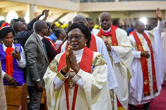 L'évêque Mujinga Kashala, les mains jointes, marche en procession à travers la foule lors de son service d'installation à la paroisse méthodiste unie Mémorial du Centenaire de Lubumbashi, en République démocratique du Congo. Photo avec l’aimable autorisation du Département de Communications de la Région Épiscopale du Sud-Congo et la Zambie.
